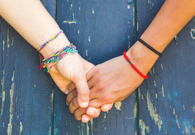 Two young people wearing bracelets are holding hands against a wooden blue background.