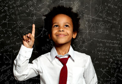 A smiling young black child stands in front of board filled with scientific formulas.