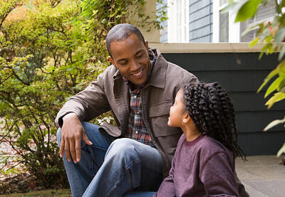 Father and daughter have a conversation while sitting on the front steps of their home. 