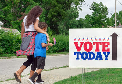 Going to Vote - a Black adult and child walking with "Vote Today" sign on sidewalk.