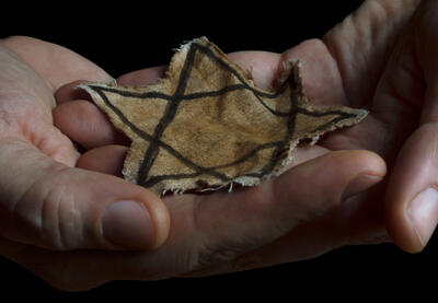 Two hands holding a faded cloth Star of David symbol.