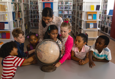 A group of young children in a school library with their teacher looking at a globe.