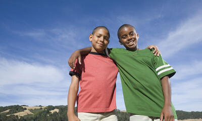 young male friends of color with arms around each other outside