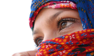 A young woman wearing a covering over her head and face looks off camera pensively