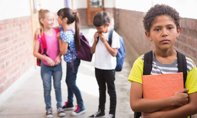 A young boy looks sad as a group of children laugh in the background