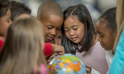 Several young kids gathered around a small globe, pointing at various spots.