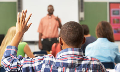 African-American student raising their hand in class, seen from behind.
