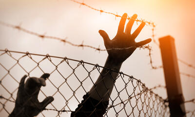 A young person's hand reaching over barbed-wire fencing.