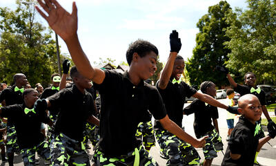 Young men of color in matching outfits dancing together outside.