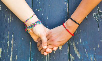 Two young people wearing bracelets are holding hands against a wooden blue background.
