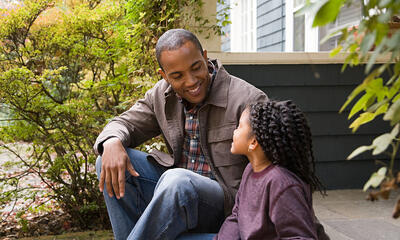 Father and daughter have a conversation while sitting on the front steps of their home. 