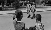 Two black children watch National Guard members patrol Central High School. 