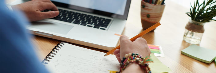 Person writing notes while looking at computer