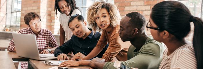 Group of professional led by woman of color gathered around documents.