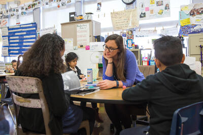 female teacher talking with students at desk