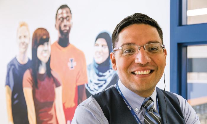 Miguel Salinas sits in front of a mural of diverse students