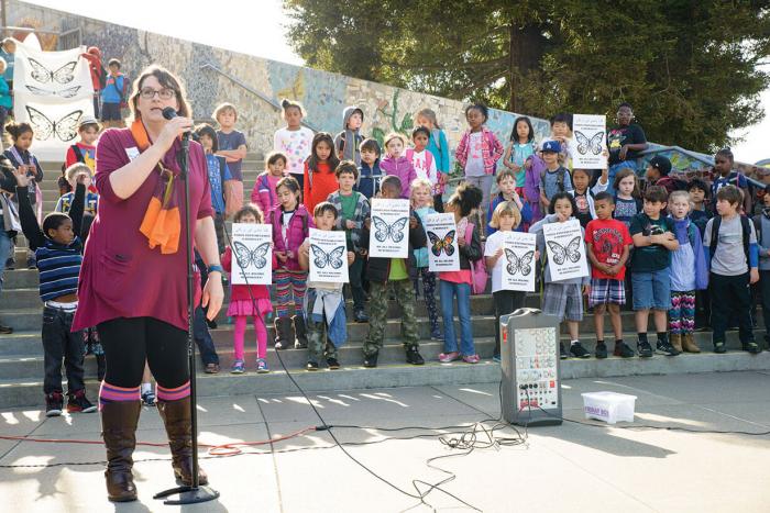 A woman speaks in front of a group of students holding up signs.