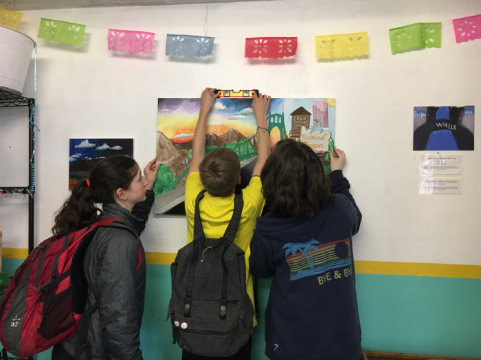 Three students hanging exhibit piece on the wall.