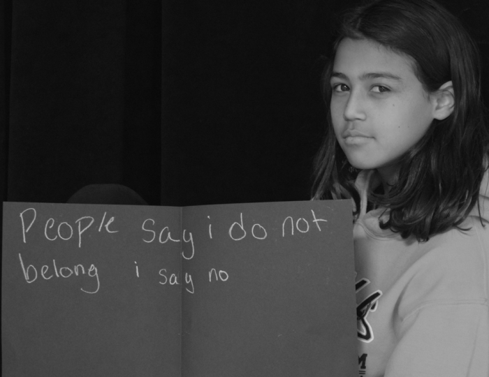 Young student holding sign that says "People say I do not belong I say no."