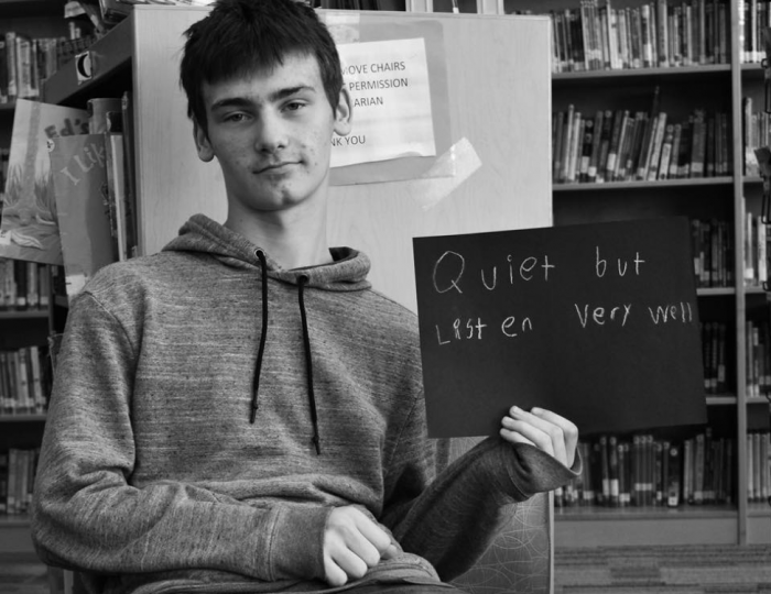 Young student holding sign that says "Quiet but listen very well."