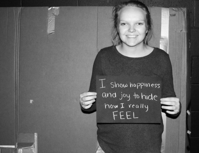 Young student holding sign that says "I show happiness and joy to hide how I really feel."