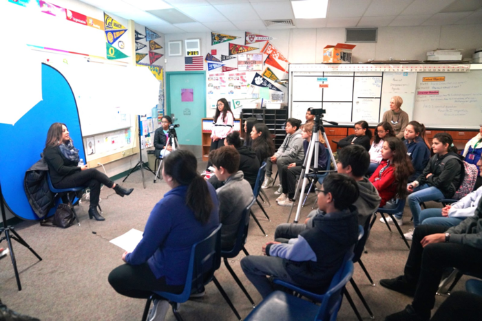 Several students in Santa Rosa classroom sitting across from interviewee, who is facing them and answering questions while being filmed.