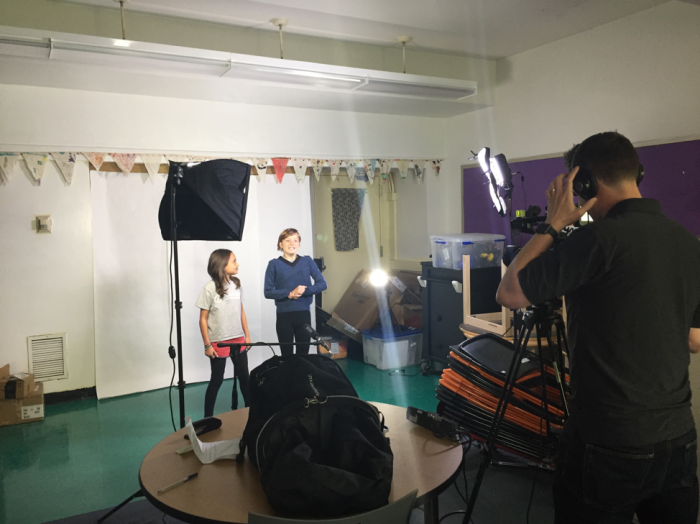 Two young students preparing to speak in front of a camera.