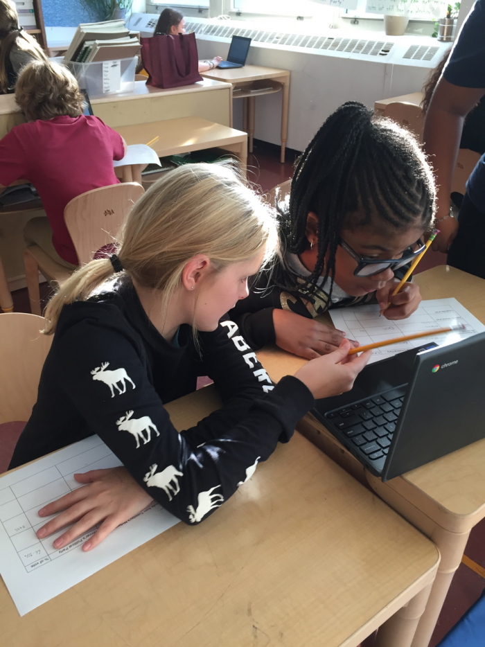 Two young students sitting and working together in front of a computer.