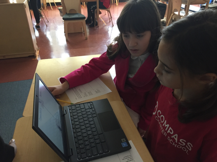 Two young students sitting and working together in front of a computer.