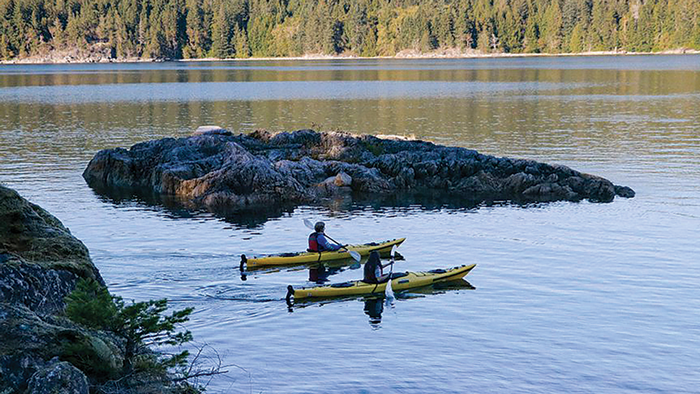 Two people in kayaks on a river, passing by an outcropping of land in the water.