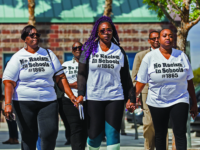 Several parents and supporters of the No Racism in Schools #1865 group marching together while holding hands.