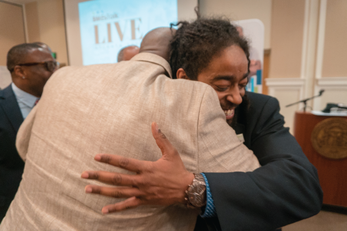 Two Black men smiling, embracing.