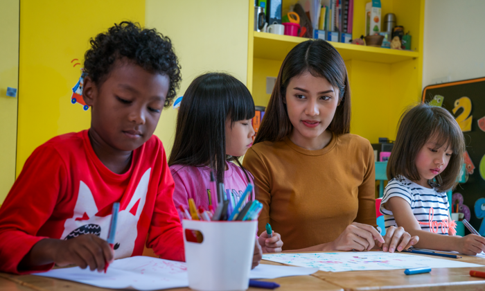 Three children sitting in an art class with their teacher.