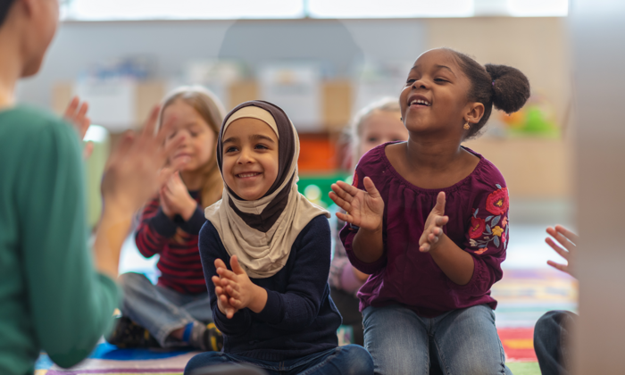 Two young girls clapping in a classroom.