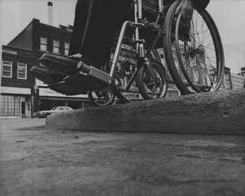 A wheelchair on top of a curb without a cut.